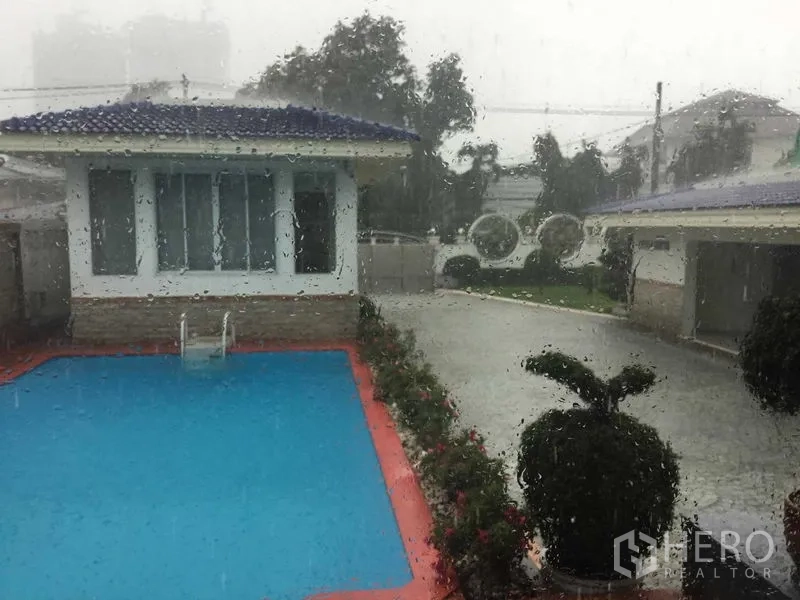 Detached House for rent or sale in Bang Kapi, Bangkok - Private outdoor swimming pool beside guest house and driveway on a rainy day.