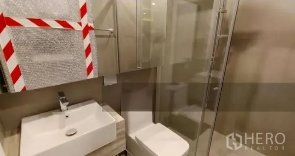 Condominium for sale - Modern condo bathroom with wall-mounted sink, mirrored cabinets and a glass shower in Ratchathewi, Bangkok.