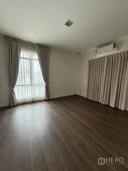 Detached House for rent in Samut Prakan - Master bedroom with wood floors, AC and soft neutral curtains.