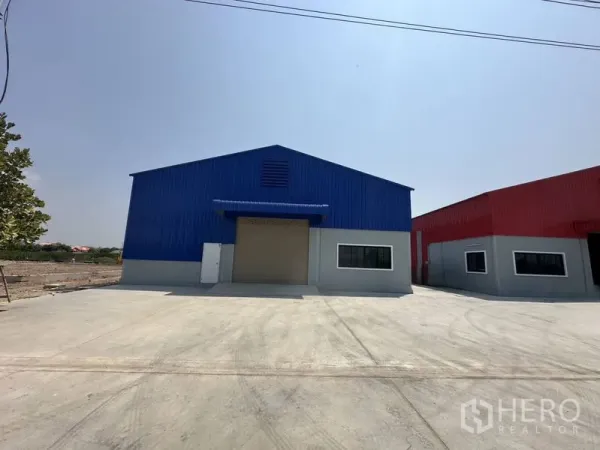 货栈 出租在Pak Kret, Nonthaburi - 蓝色钢结构仓库正面，配有大型卷闸门与宽阔的混凝土地坪。