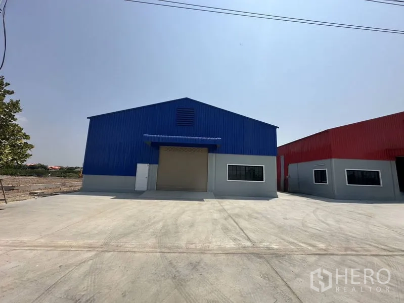 คลังสินค้า ให้เช่าในPak Kret, Nonthaburi - มุมมองด้านหน้าโกดังสีน้ำเงิน ประตูม้วนใหญ่ พร้อมลานคอนกรีตกว้าง