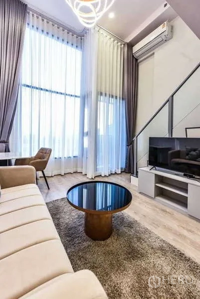 Condominium for rent in Huai Khwang, Bangkok - Living area with floor-to-ceiling curtains, TV console and round coffee table.
