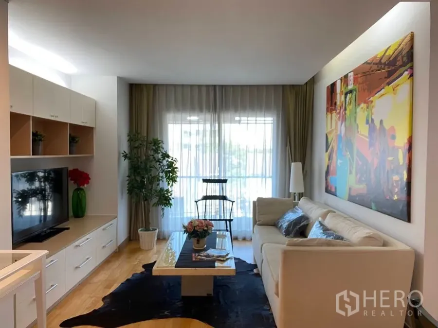 Condominium for rent or sale in Phra Khanong, Bangkok - Bright living room with cream sofa, TV cabinet, large artwork and sheer curtains opening to a balcony.