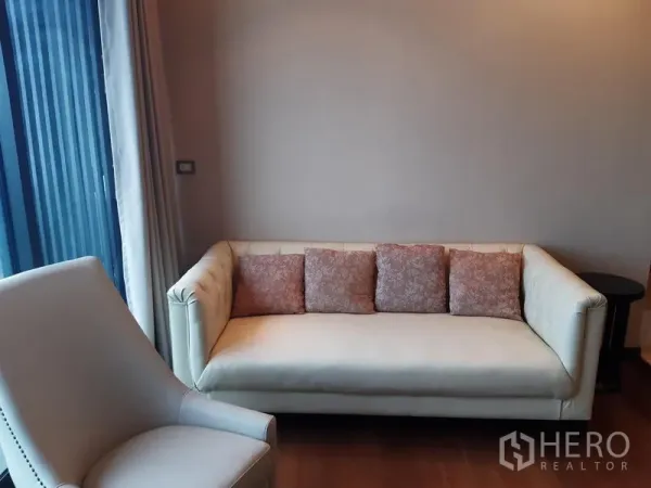 公寓 出租或出售在Khlong Toei, Bangkok - 休闲角落，奶油色沙发与花纹抱枕，旁为窗帘墙。