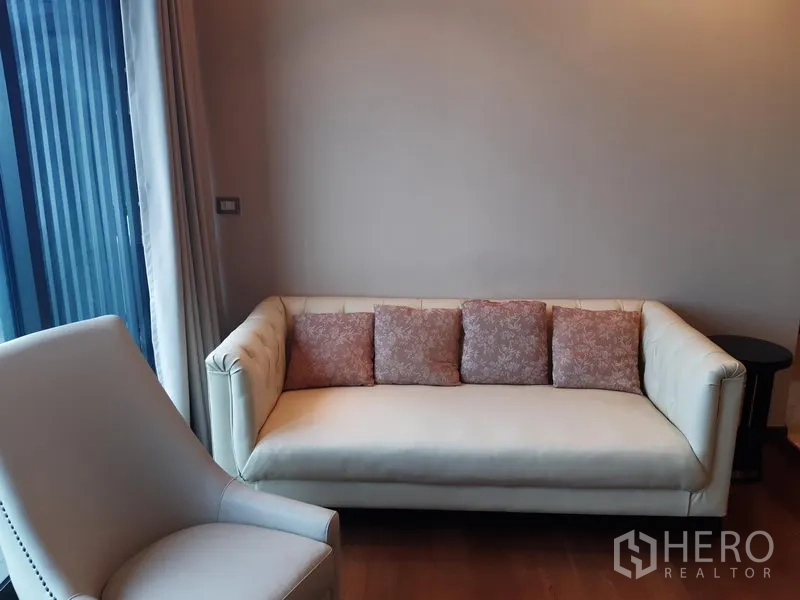 公寓 出租或出售在Khlong Toei, Bangkok - 休闲角落，奶油色沙发与花纹抱枕，旁为窗帘墙。