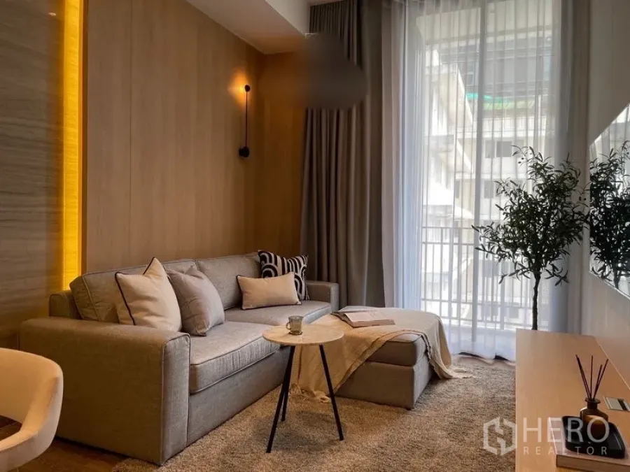 คอนโด ให้เช่าหรือขายในPathum Wan, Bangkok - ห้องนั่งเล่นสว่างเฟอร์นิเจอร์โทนเทา โซฟาเบด โต๊ะกลม และผ้าม่านโปร่งสูงจรดเพดานเปิดออกสู่ระเบียง