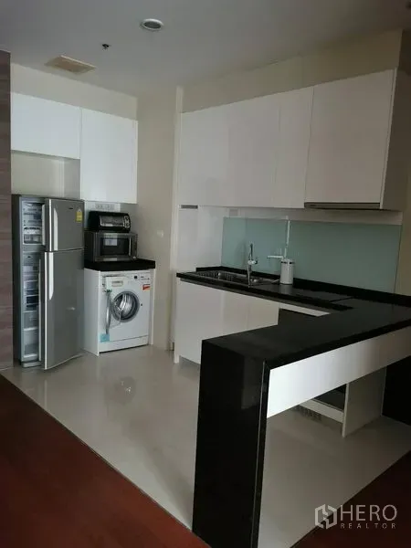 公寓 出租在Khlong Toei, Bangkok - 公寓厨房，白色橱柜与黑色吧台，配冰箱、烤箱和洗衣机，位于空堤区曼谷