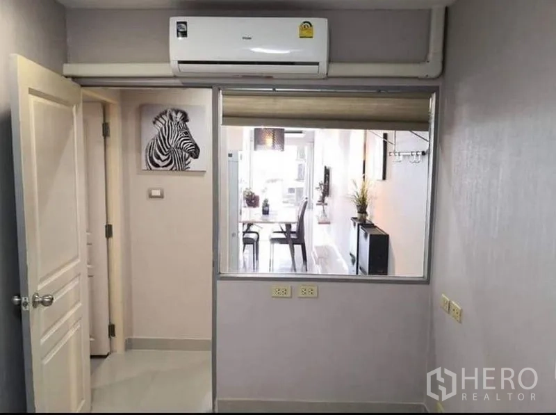 公寓 出售在Khlong Toei, Bangkok - 带壁挂空调的小房间，内窗可见餐厅，灰色墙面与电源插座。