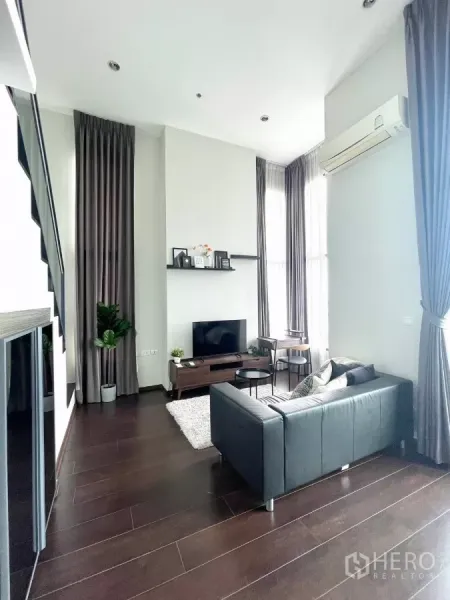 Condominium for rent in Watthana, Bangkok - Spacious lounge with black leather sofa, area rug, and high ceilings viewed from the entry.
