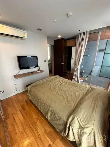 Condominium for sale in Bang Rak, Bangkok - Bedroom with wall-mounted TV, wood floors and glass partition to outdoor area.