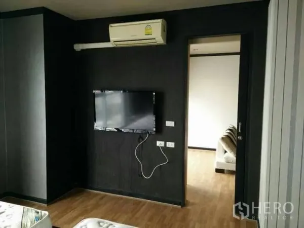 Condominium for rent in Ratchathewi, Bangkok - Living area in a Bangkok condo with wall‑mounted TV, air conditioner and wood flooring.