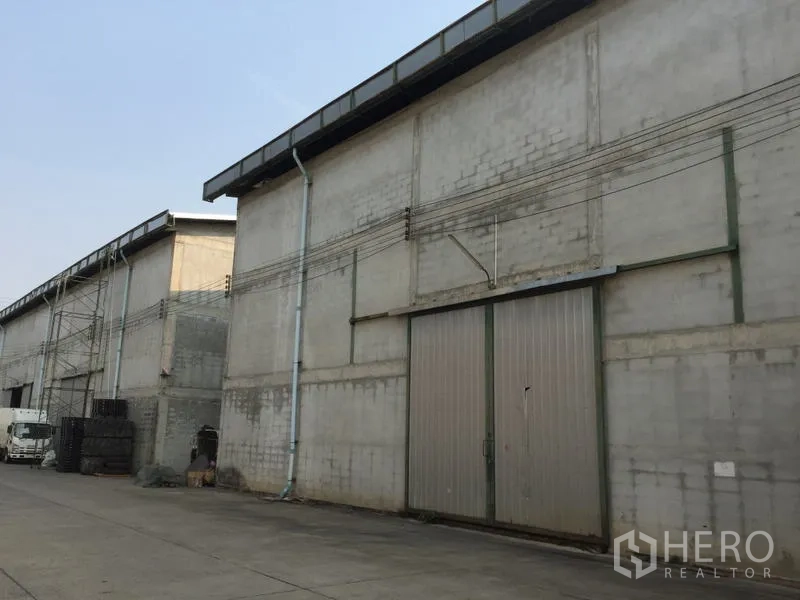 Warehouse for rent in Mueang Pathum Thani, Pathum Thani - Warehouse facade with tall sliding metal door and visible service conduits along the wall.