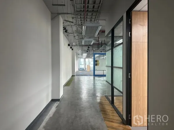 Office Space for rent in Bang Rak, Bangkok - Long hallway in a modern office with exposed ceiling services and a glass partition on the right.