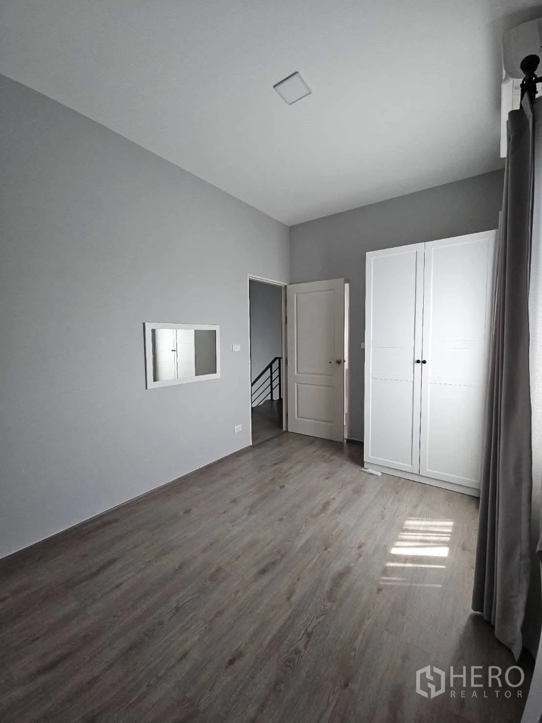 Detached House for rent in Bang Phli, Samut Prakan - Bright bedroom with grey walls, wood floors, white wardrobe and a small window mirror.