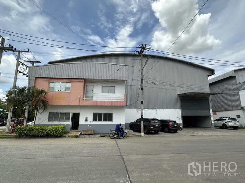 工厂 出租在Phra Nakhon Si Ayutthaya - 带办公室阳台的立面，车道与多处停车位通往卷闸门入口。