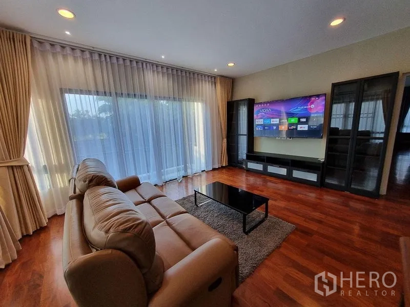 Detached House for rent in Bang Khae, Bangkok - Upstairs family room with leather sofa, media wall, and floor-to-ceiling curtains.