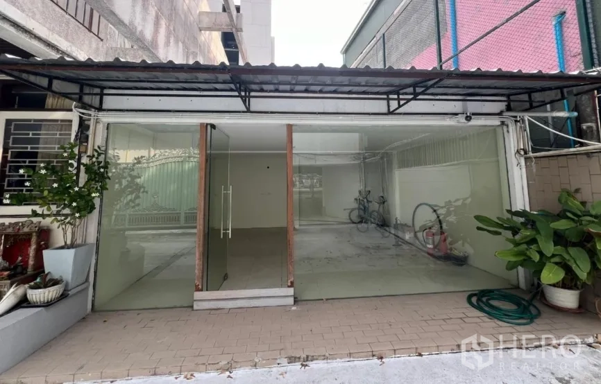 零售空间 出租在Watthana, Bangkok - 一层商铺立面，大片玻璃橱窗与摆放的盆栽。