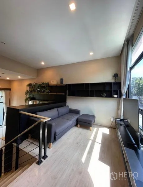 Townhouse for rent in Yan Nawa, Bangkok - Mezzanine lounge with sectional sofa, media shelf, and tall windows.