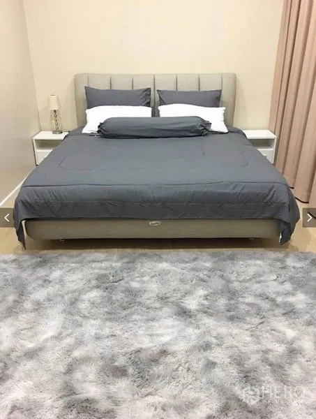 Townhouse for rent or sale in Suan Luang, Bangkok - Primary bedroom with upholstered bed, gray bedding, bedside tables, and large rug.
