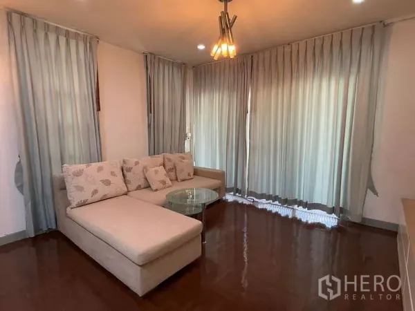 Detached House for rent in Bang Kapi, Bangkok - Cozy lounge with L‑shaped beige sofa, glass coffee table and full‑height curtains.