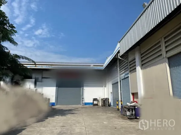 Factory for rent in Lam Luk Ka, Pathum Thani - Exterior loading yard with multiple roll‑up doors and wide concrete apron beside the factory building.