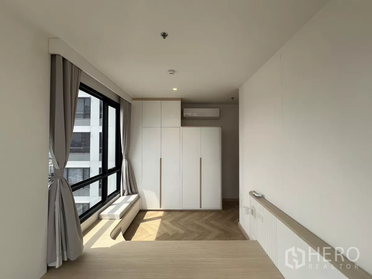 Condominium for rent or sale in Chatuchak, Bangkok - Bedroom with large wardrobes and a window seat, grey curtains and abundant natural light.
