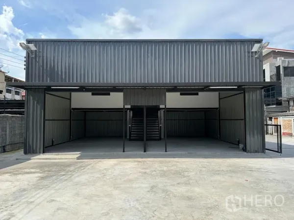 Warehouse for rent - Front view of metal-clad warehouse with central staircase, open bays and expansive driveway.