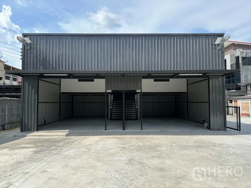 Warehouse for rent - Front view of metal-clad warehouse with central staircase, open bays and expansive driveway.