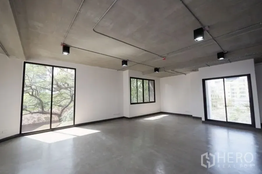 Office Space for rent in Watthana, Bangkok - Bright corner office with three large windows, exposed ceiling fixtures, and natural light.