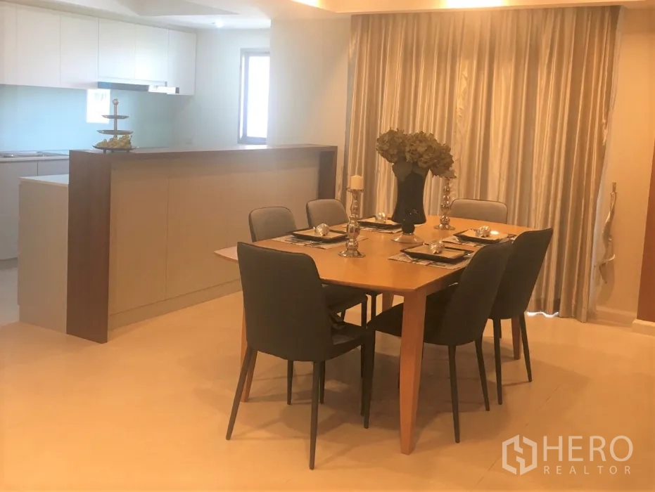 Condominium for rent in Watthana, Bangkok - Six-seat dining table next to a breakfast bar and a light-toned kitchen with ample cabinetry.