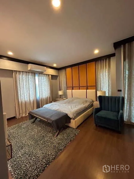 Detached House for rent in Bang Kapi, Bangkok - Bright bedroom with bed, accent chair, sheer curtains and warm wood flooring.