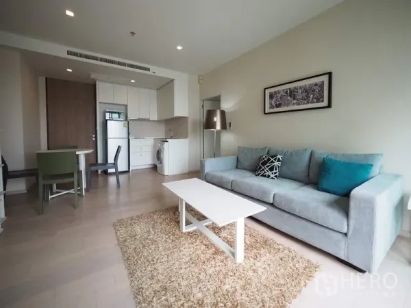 Condominium for rent in Watthana, Bangkok - Open-plan living area with sofa, coffee table, and compact fitted kitchen.