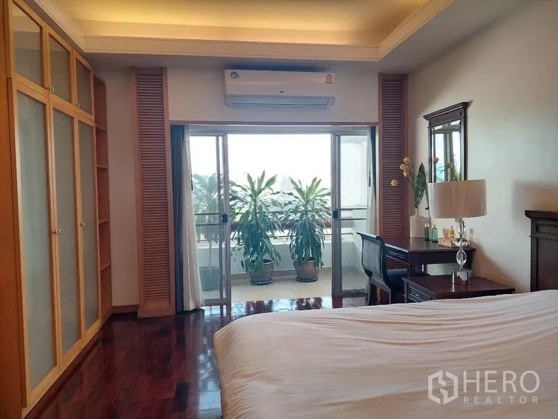 อพาร์ทเมนท์ ให้เช่า - ห้องนอนใหญ่ ตู้เสื้อผ้าบิลต์อิน โต๊ะทำงาน และประตูกระจกสู่ระเบียงที่มีต้นไม้