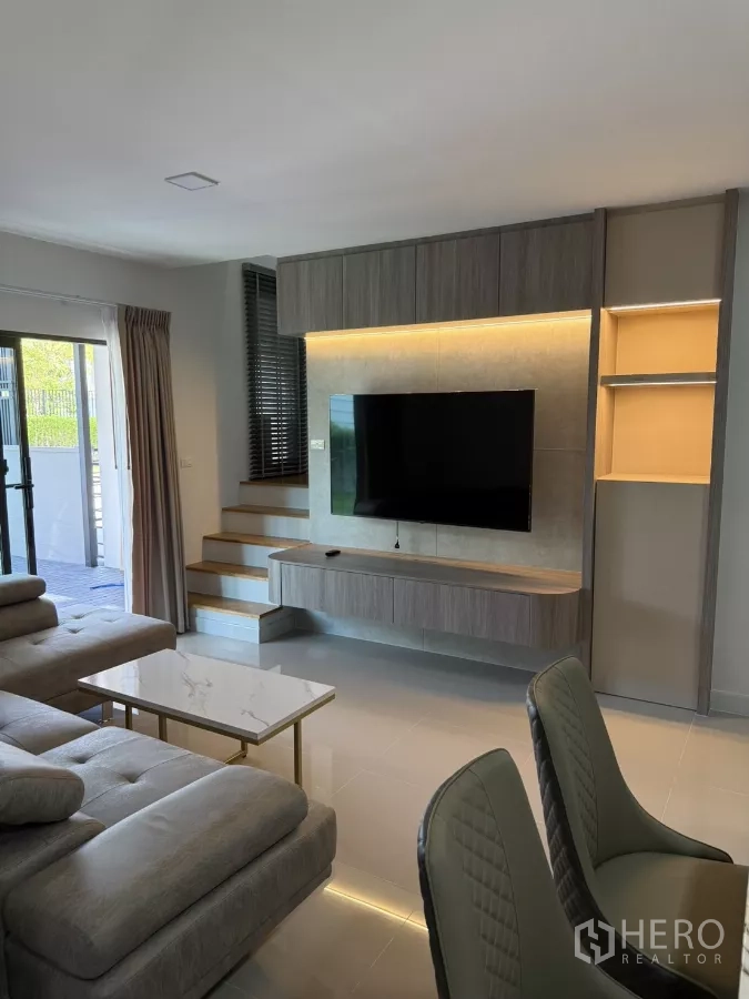 Townhouse for rent or sale in Bang Phli, Samut Prakan - Bright living room with built-in TV wall, sectional sofa and stairs.