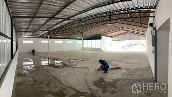 货栈 出租在Mueang Pathum Thani, Pathum Thani - 大型仓库通道正在清洁，宽跨金属屋顶、通风砖窗与支柱布局。