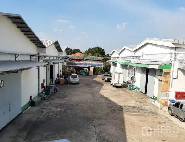 货栈 出租在Suan Luang, Bangkok - 一排低层仓库带卷帘门，货车停靠在宽阔服务通道