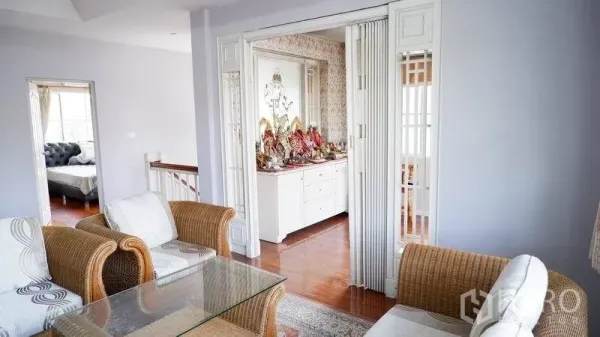 Detached House for rent in Prawet, Bangkok - Bright sitting area with wicker sofas, glass coffee table and folding doors to a built-in display cabinet.