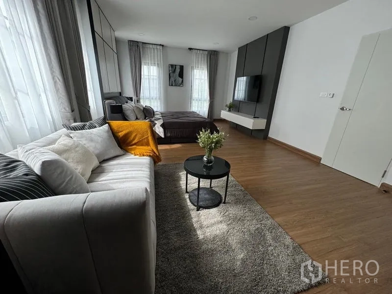 Detached House for rent or sale in Bang Phli, Samut Prakan - Daylight master suite with sofa seating, textured rug and wall‑mounted TV unit.