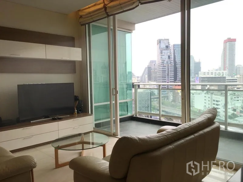 Condominium for rent or sale in Bang Rak, Bangkok - TV area facing floor-to-ceiling glass doors leading to a balcony and urban skyline.
