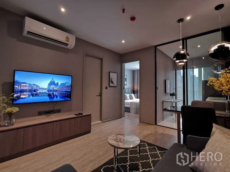 คอนโด ขายในWatthana, Bangkok - ห้องนั่งเล่นปูพื้นไม้ ทีวีติดผนัง ประตูกระจกสู่ครัวและระเบียง วิวเมือง