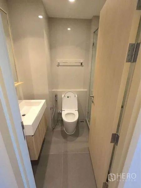 Condominium for rent in Watthana, Bangkok - Compact bathroom with white sink, toilet, and light-wood vanity.