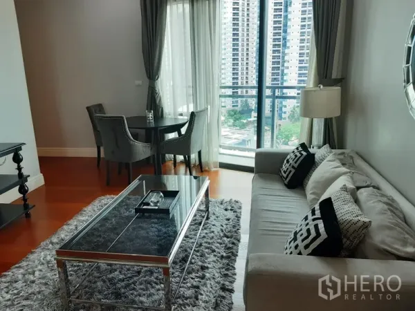 คอนโด ให้เช่าหรือขายในKhlong Toei, Bangkok - ห้องนั่งเล่นสว่าง โซฟาสีเทา โต๊ะกระจก มุมทานอาหาร ข้างหน้าต่างบานสูงและระเบียงวิวเมือง