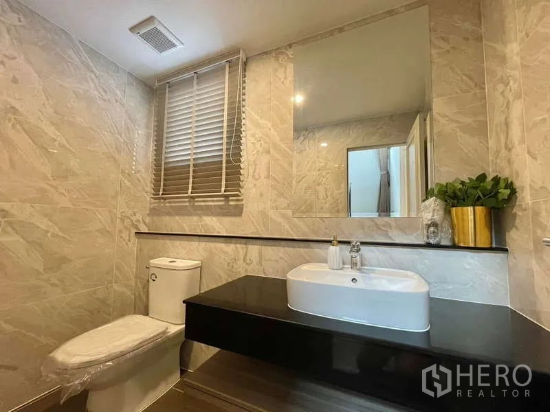 Detached House for rent in Bang Phli, Samut Prakan - Powder room with marble-effect tiles, vanity mirror and toilet.