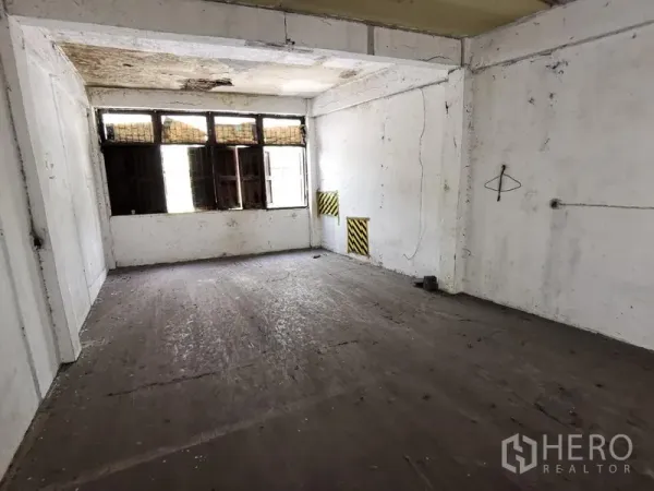 Home Office for rent in Khlong Toei, Bangkok - Empty room with concrete floor and high windows, ideal for renovation.