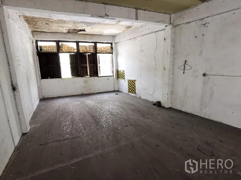 Home Office for rent in Khlong Toei, Bangkok - Empty room with concrete floor and high windows, ideal for renovation.