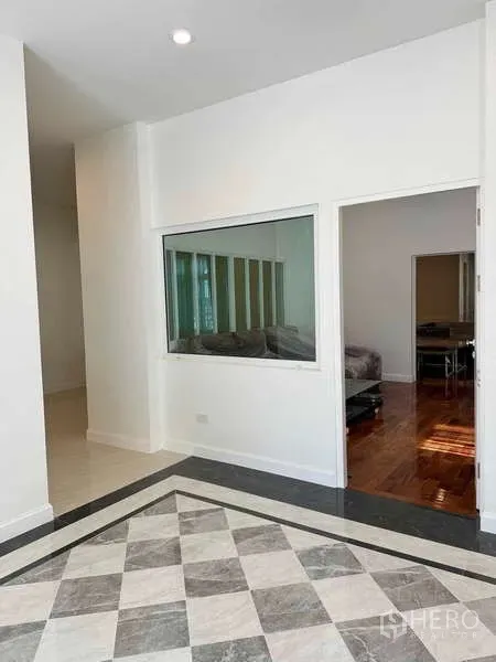 Detached House for rent in Samut Prakan - Entrance foyer with checkered marble floor and an interior window looking into a sitting room.