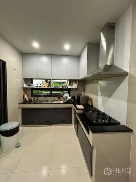 Detached House for rent in Bang Kapi, Bangkok - L-shaped kitchen with gas hob, range hood, glossy cabinetry and tiled floor.