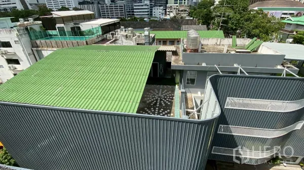 独立商业地产 出租在Bang Rak, Bangkok - 屋顶与庭院景观，绿色金属屋面、蓄水罐与马赛克铺地，周围中高层城市景致。