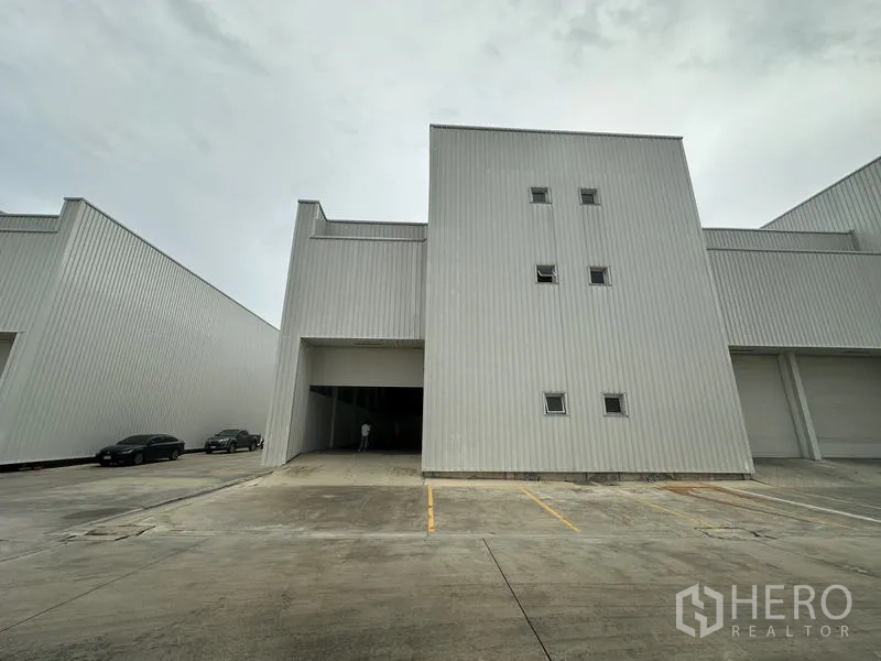 工厂 出租在Khlong Luang, Pathum Thani - 工业厂房立面，配高卷闸门与划线停车位。