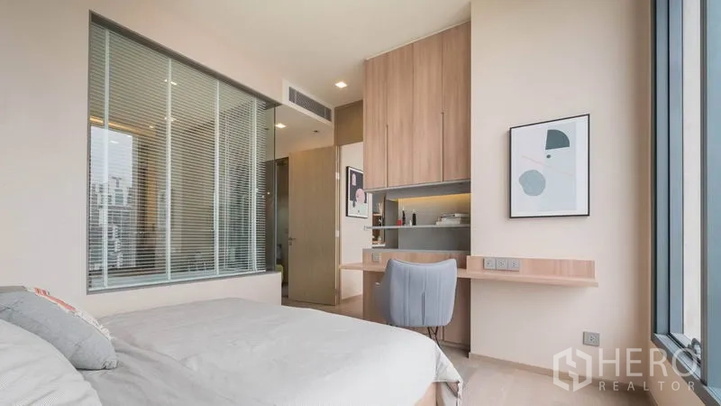 Condominium for rent in Watthana, Bangkok - Master bedroom with large window, built-in desk and wardrobe, and a view into the bathroom through a glass wall.
